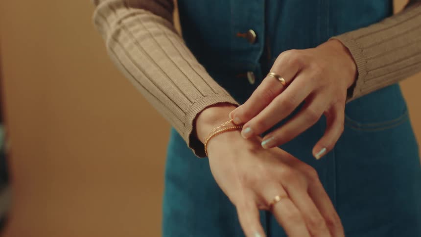 A woman in a denim dress adjusting a gold bracelet
