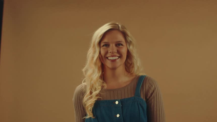Woman wearing overalls with jewelry and is smiling