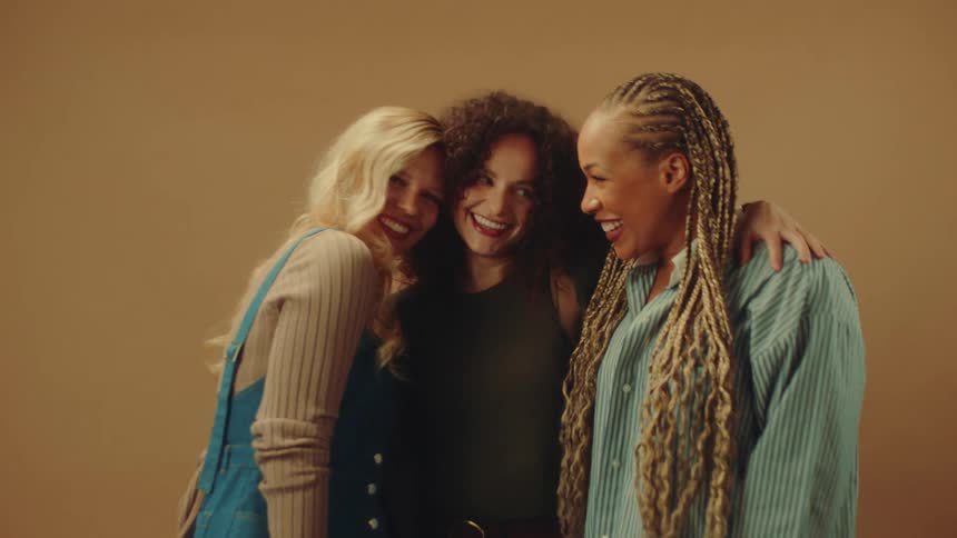 Three smiling women posing together against a solid brown background