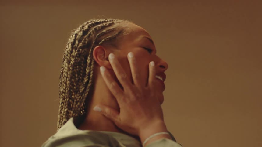 Woman with multiple long hair braids strokes her hand down her face