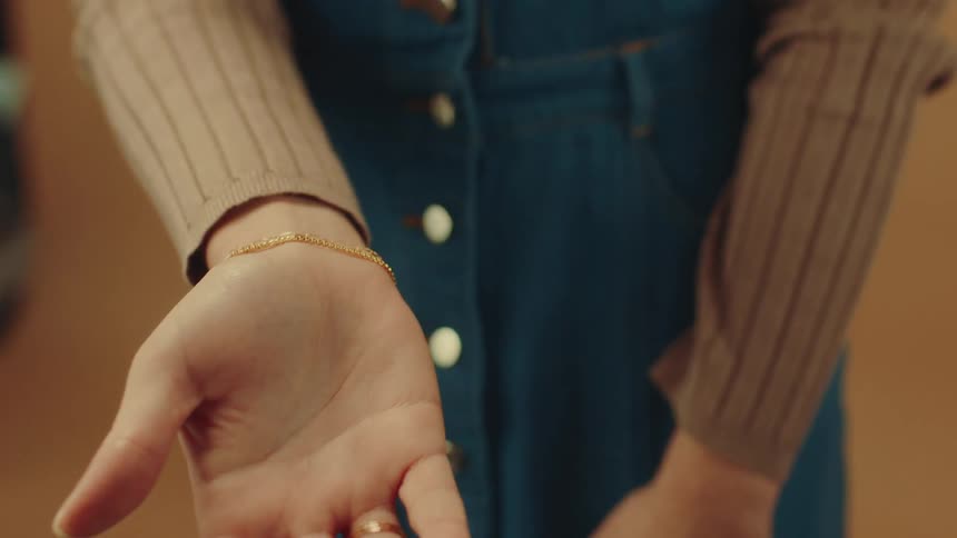 Close up of the hands of a woman modeling gold bracelets and rings against a beige background