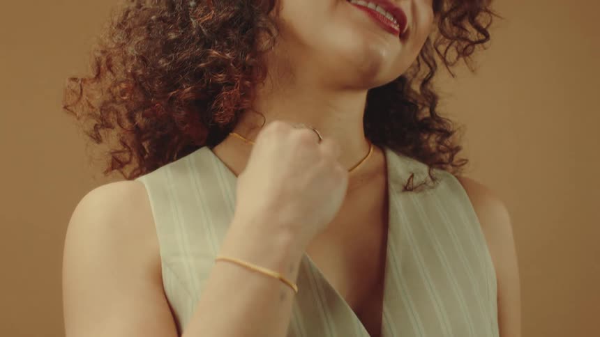 Woman in a fashionable outfit touches her necklace while wearing a matching bracelet