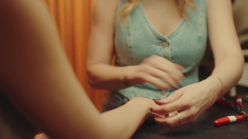 A woman adjusting a thin gold chain on another persons wrist