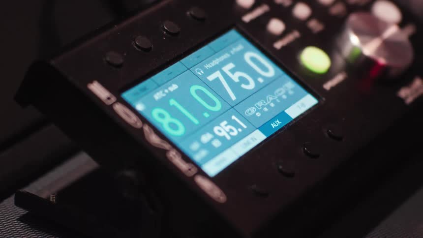 A closeup shot of a grace design m908 monitor controller displays a digital readout with numbers and text on a light blue screen
