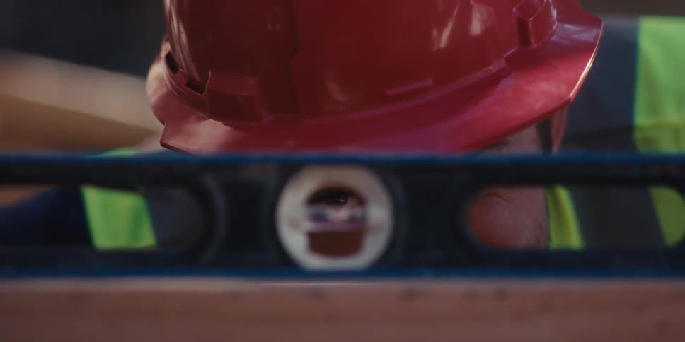 Worker with protective helmet looking through a level tool