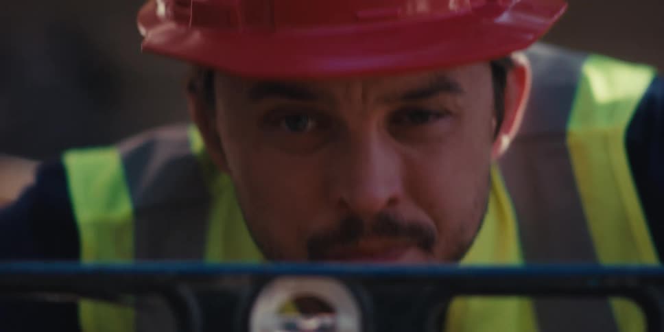 A construction worker wearing a visibility vest and red hard hat uses a level at a construction site