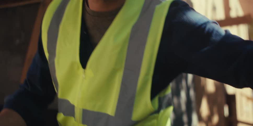 Man wearing a helmet on a construction site measuring the length of a wooden slat with a tape measure