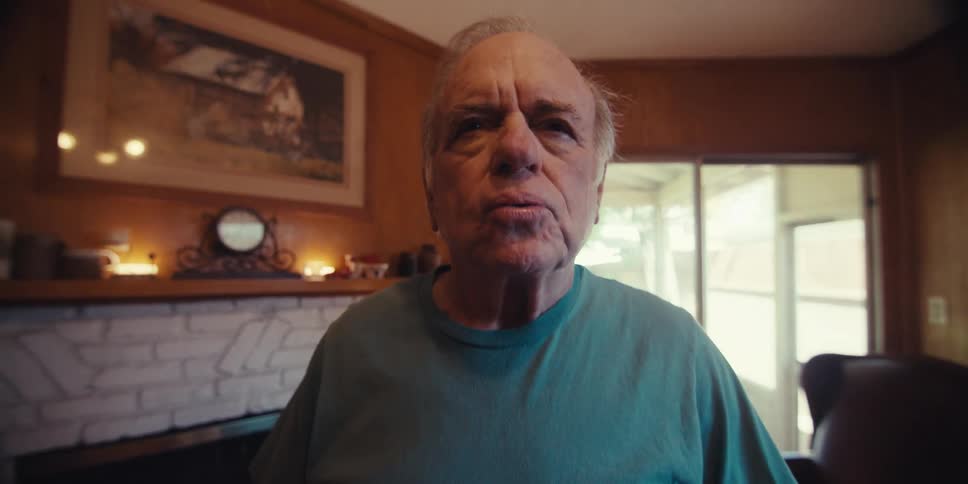 An elderly man stands on the living room practicing breathing exercises with sunlight streaming through the windows