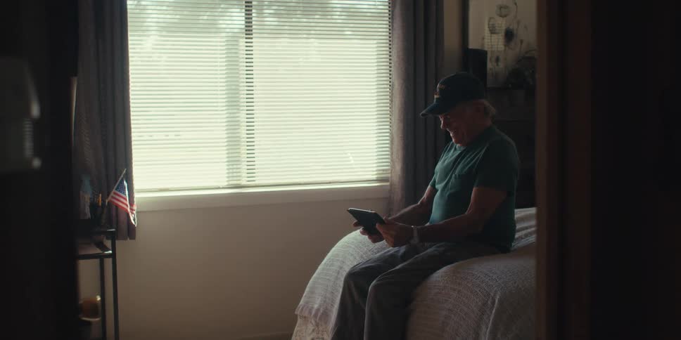 Elderly man sitting on bed in a bedroom and using a tablet