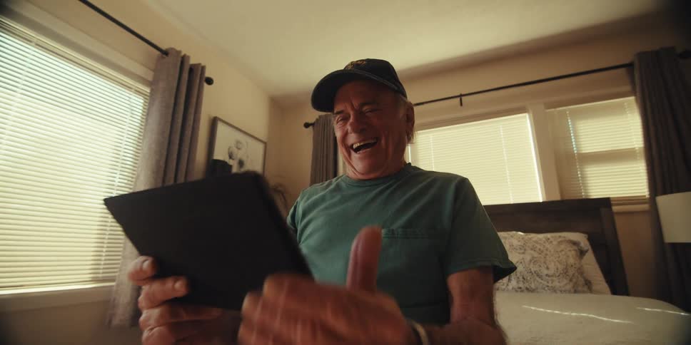 A man tilts his head back laughing while looking at a tablet