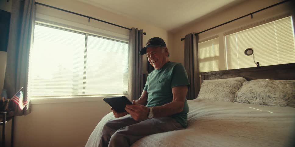 A man is laughing while looking at his tablet