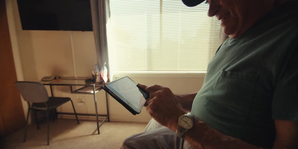 Elderly man sitting on bed having fun using a tablet