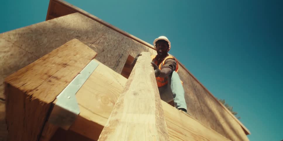 A laborer passes a board down to a coworker