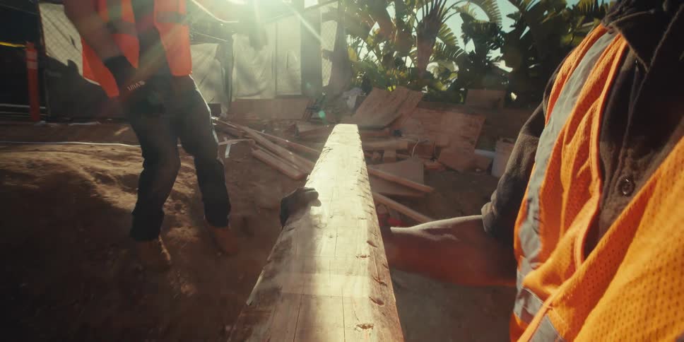 Two men carrying a wooden slat on a construction site