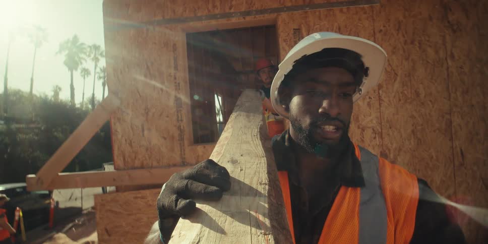 Construction workers carry lumber and work on a building project on a sunny day