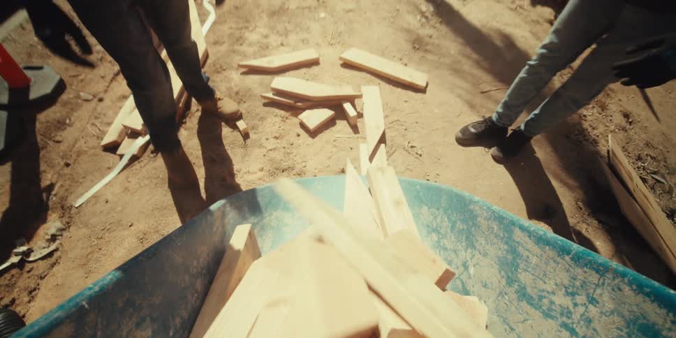 Workers empty the wood from the wheelbarrow then toss their hard hats