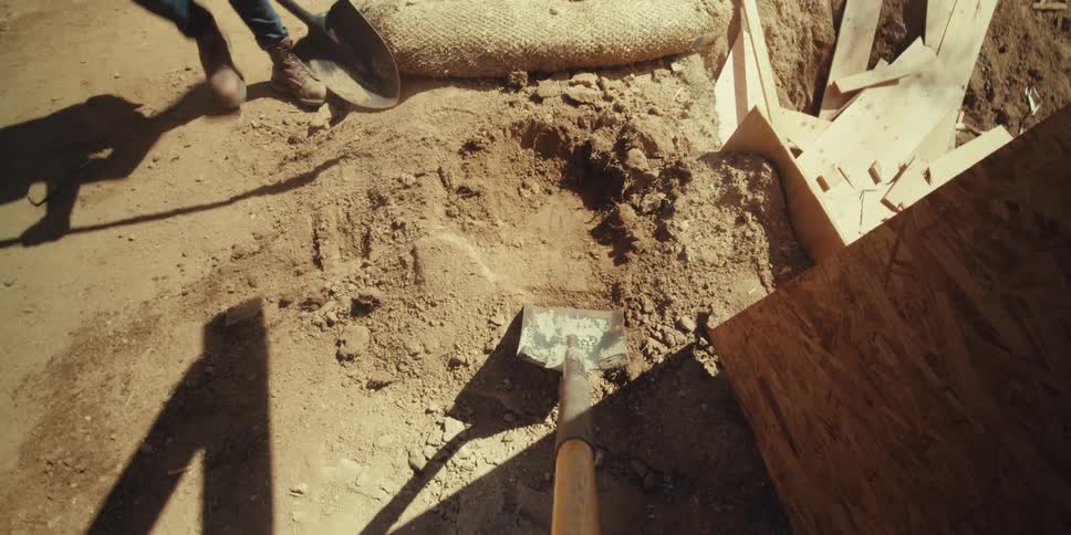 Construction workers shovel dirt into a wheelbarrow at a construction site