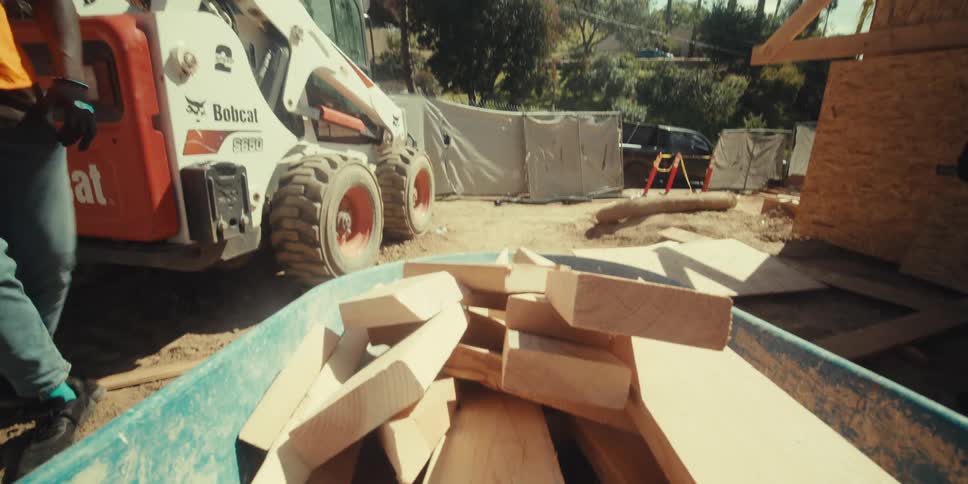 Construction workers place scrap lumber in a wheelbarrow while working on a construction site on a sunny day