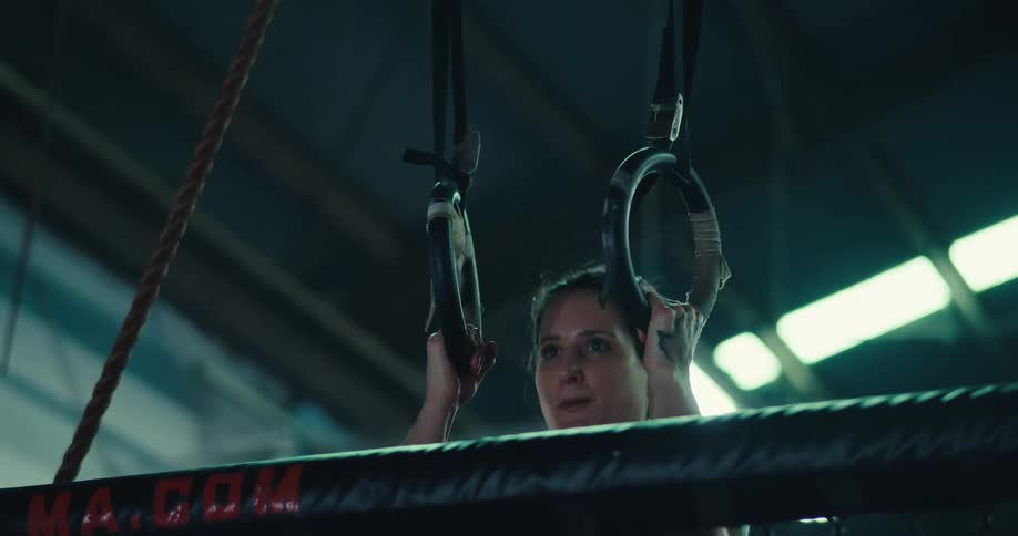 A tattooed individual performs a pullup on gymnastic rings in an indoor gym