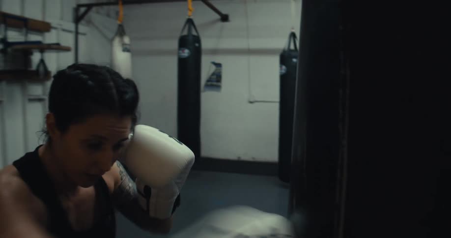 Woman with boxing gloves practicing punches against a punching bag in a gym