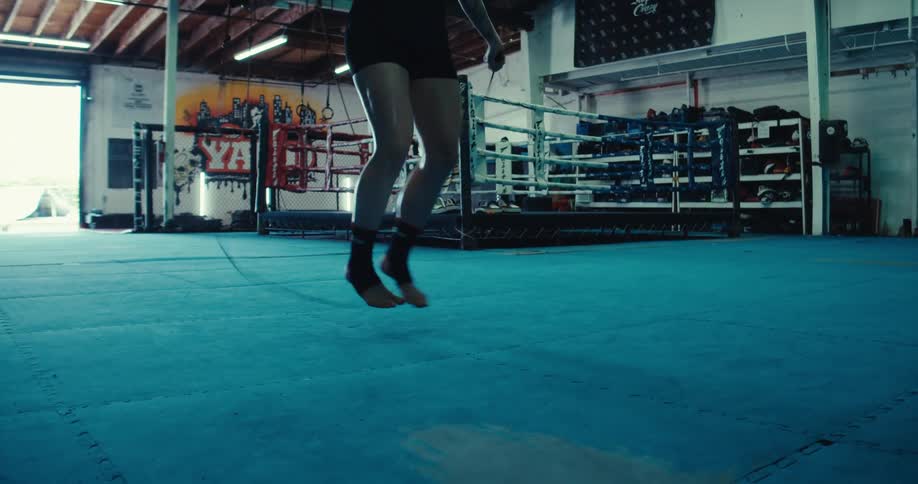 A woman is intensely focused as she rhythmically jumps and swings a skipping rope on a brightly colored wrestling mat