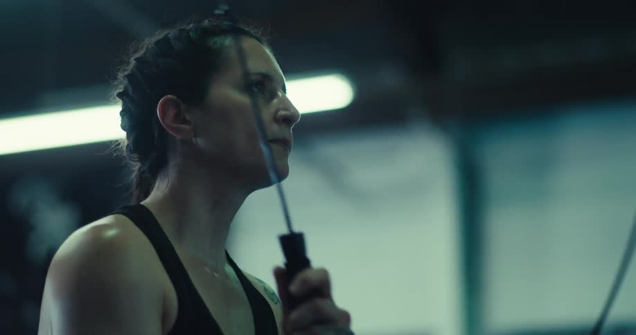 A woman with braided hair intensely jumps rope in a gym