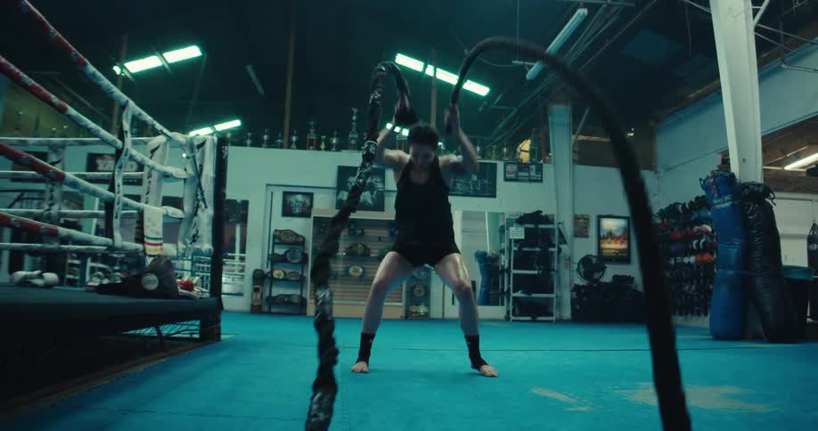 Female athlete training with battle ropes in boxing gym