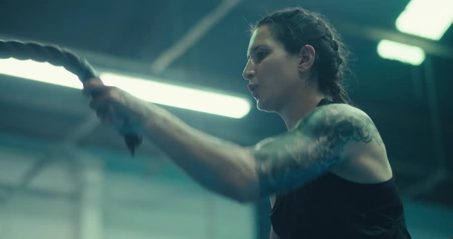 A woman performs battle rope exercises in a gym vigorously moving the ropes in alternating waves