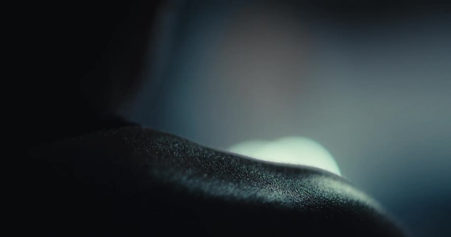 A closeup captures a bare shoulder glistening under soft light in a dimly lit setting
