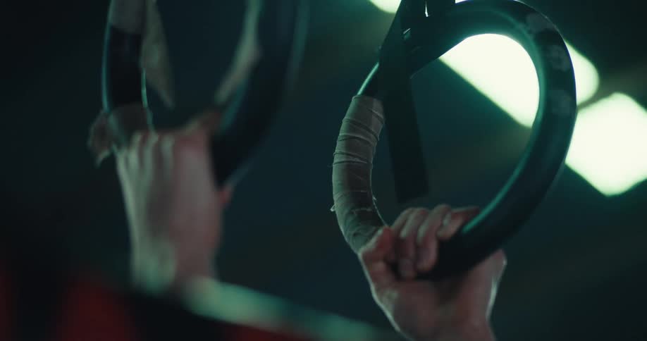 A woman is doing pullups on rings in a gym