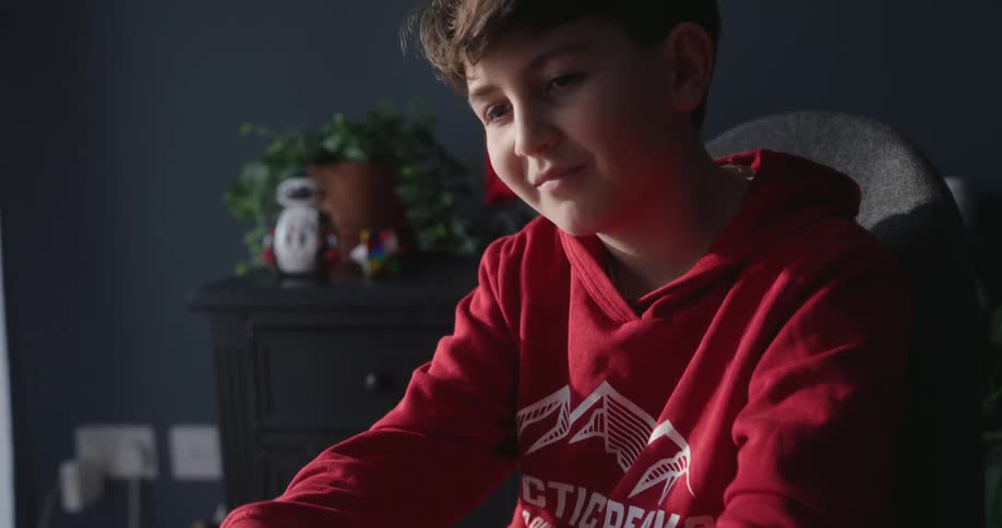 Boy sitting at a table typing on a laptop