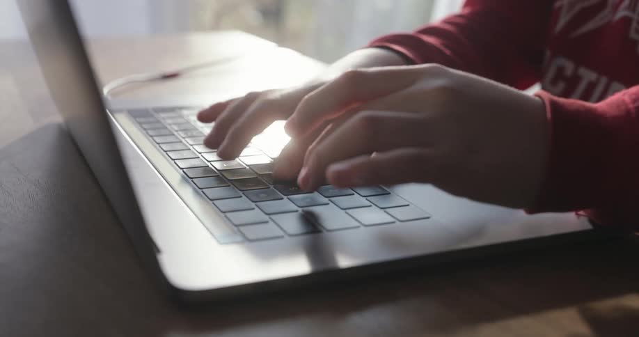 Hands of a boy typing on a laptop