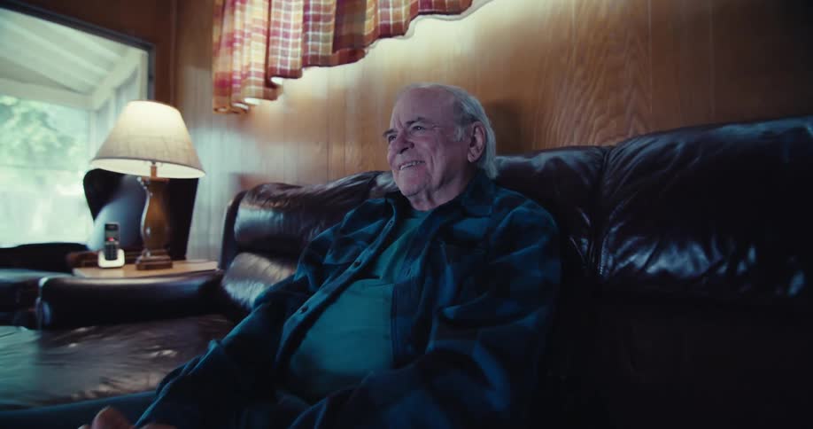 A footage of an elderly man sitting on a black sofa and laughing