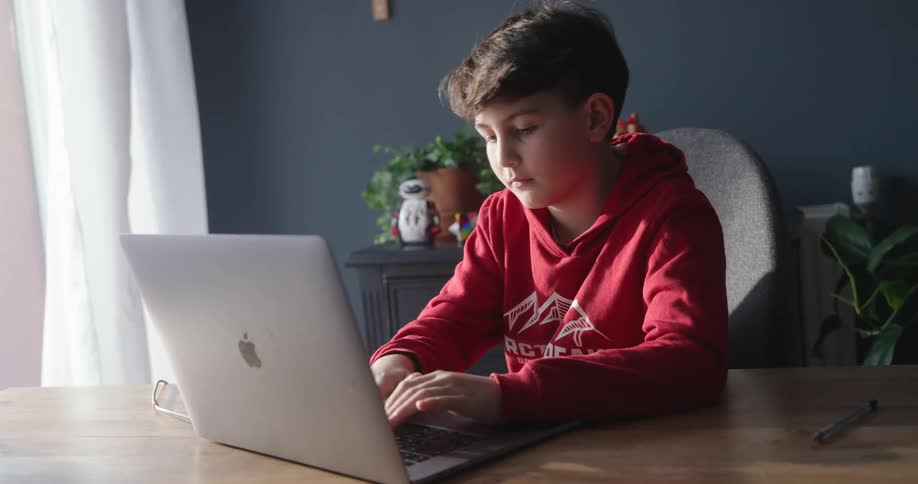 Boy in red sweatshirt sitting typing on a laptop