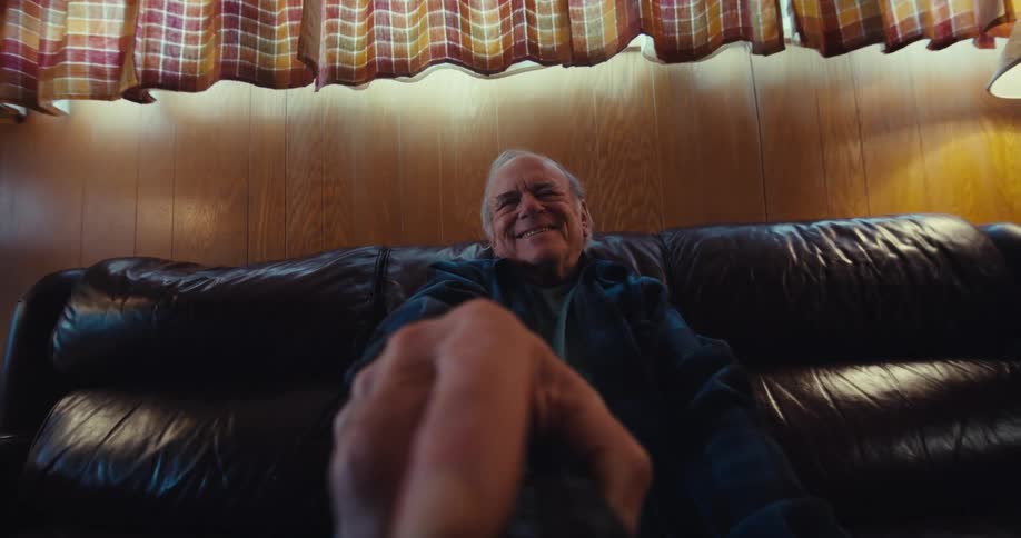 An elderly man sitting on a couch at home using a tv remote