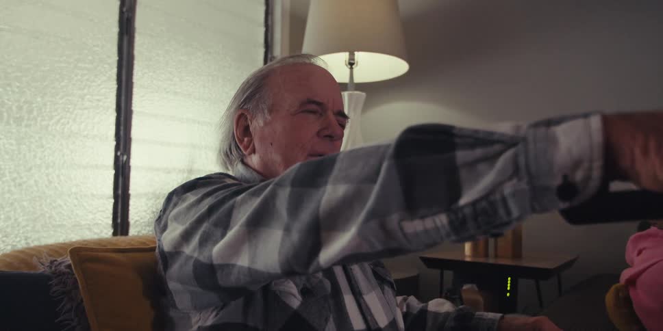 An elderly couple sits on the couch while the husband pushes buttons on a tv remote