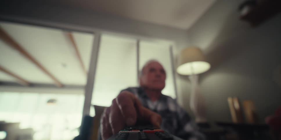Elderly man picking up a television remote control and pressing the buttons