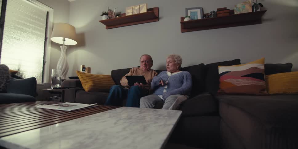 A couple talk while pointing at a tablet on the couch