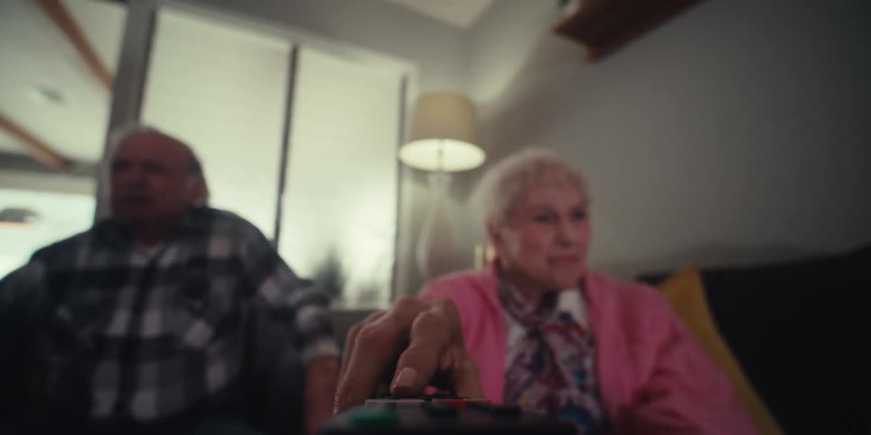 An elderly couple are pressing buttons on a remote but arent succeeding in doing what they want to do they look frustrated the camera is mounted to the remote
