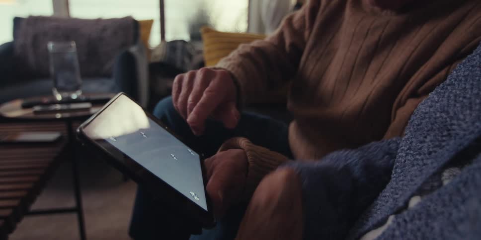 A close up of a couple of elderly people seated on a couch in the living room using a tablet together