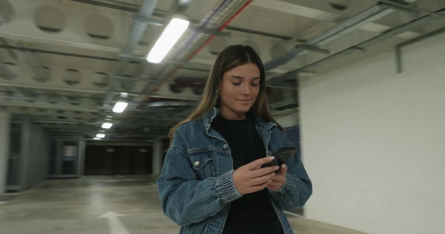 Young girl standing in an indoor parking structure texting on a cell phone