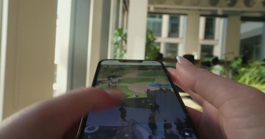 Woman with manicured fingernails scrolls on her smartphone in a room filled with plants