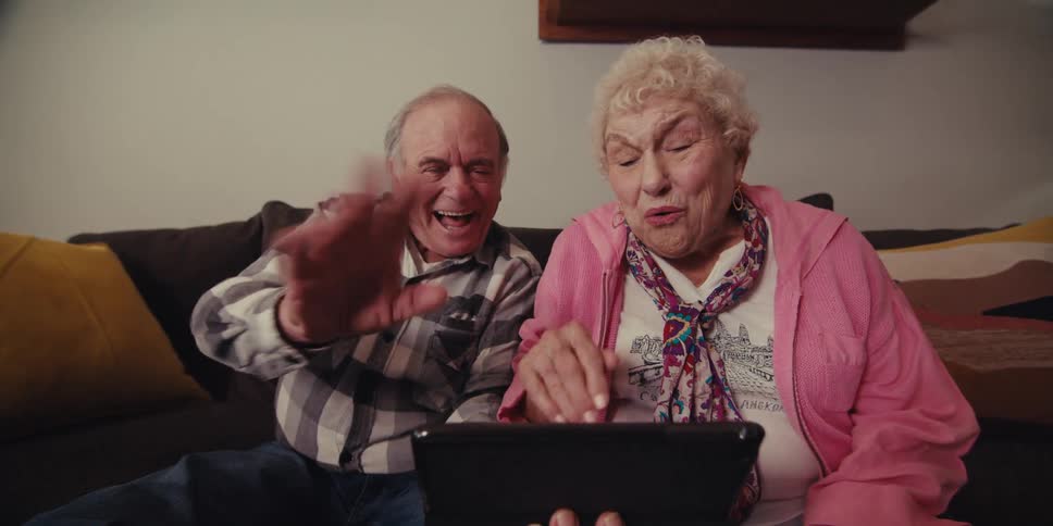 Happy elderly couple waving and giving kisses while face timing on a tablet