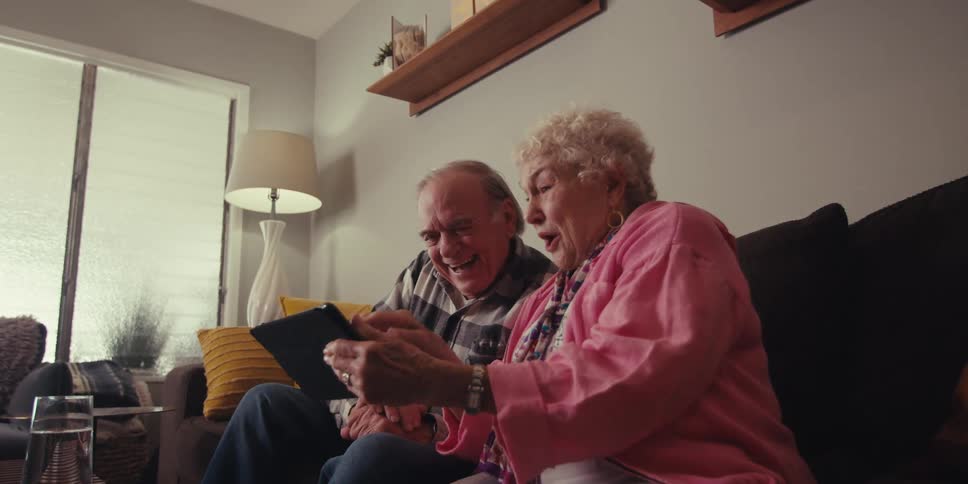 Happy elderly couple talking and interacting with tablet