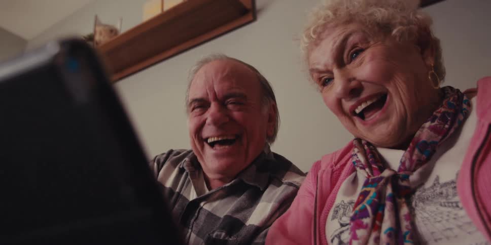 A man and woman lean forward laughing at the tablet