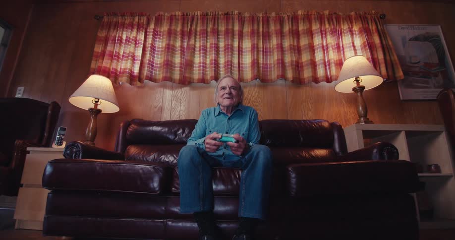 Elderly man playing a video game with a controller while sitting on a sofa