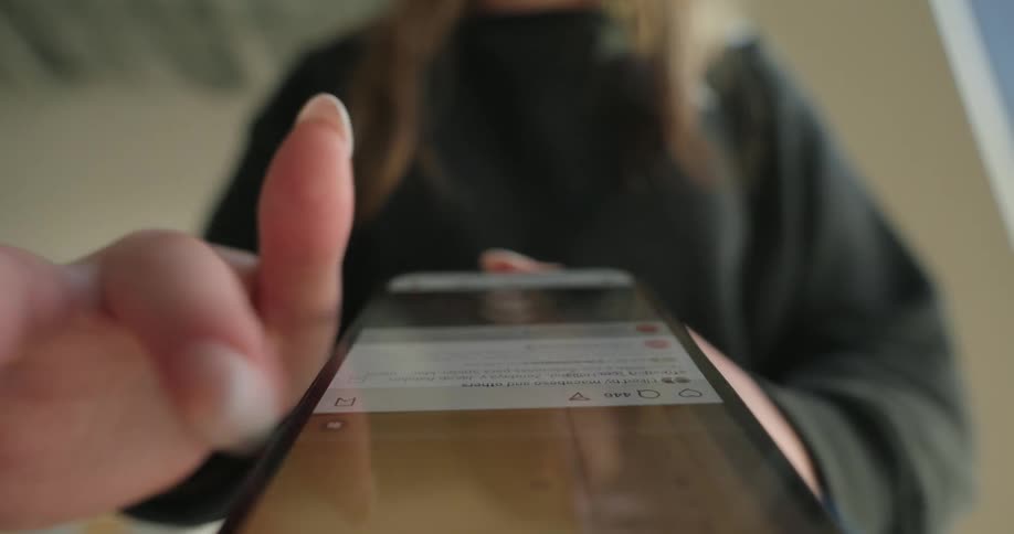 A womans hands swiping on a smartphone screen with the focus on the screen and fingers and the womans face slightly blurred in the background