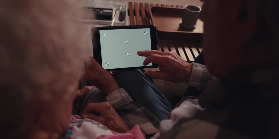 Elderly man and woman sit on the couch and use tablet by the coffee table