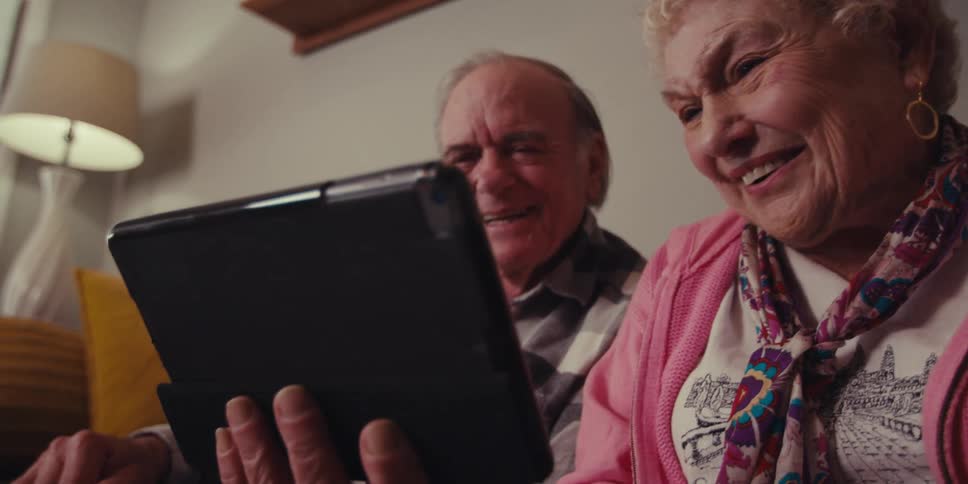 Two grandparents video chatting on a tablet with some family members and are happy