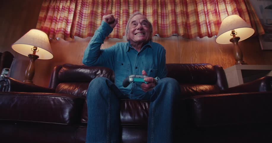 Elderly man cheering happily while holding a wireless video game controller